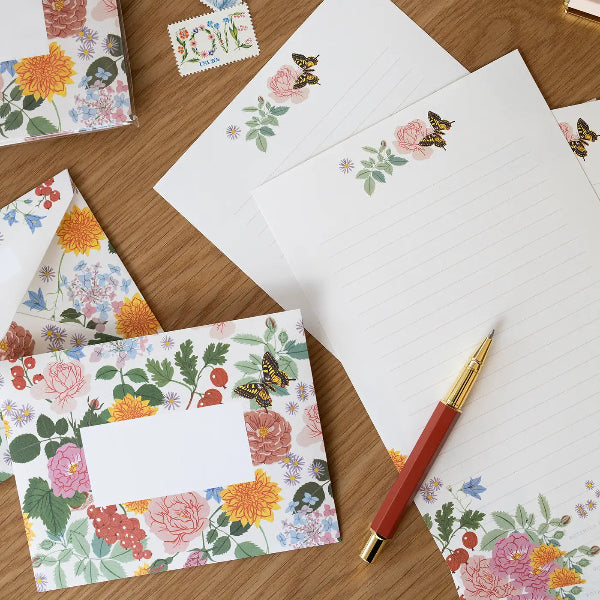 Floral stationery set with envelopes, postcards, and a pen on a wooden surface.