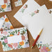 Floral stationery set with envelopes, postcards, and a pen on a wooden surface.
