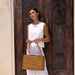 Woman holding a woven bag in front of a wooden door with intricate carvings