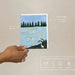 Hand holding a plantable seed paper envelope with nature-themed illustration on a beige background