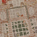 Close-up of a detailed embroidered textile featuring a brick wall background, multiple window panels, green garlands, bears, and small decorative motifs in beige, brown, green, and orange tones.