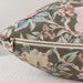 A close-up of a decorative throw pillow with a floral print in muted green, pink, cream, and blue, featuring a gold zipper.