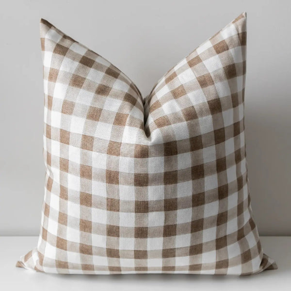 A square throw pillow with a brown and white gingham check pattern, photographed against a neutral light gray background.
