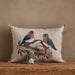 Decorative pillow with embroidered design of birds and a nest on a wooden surface.