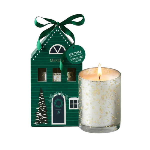 A Christmas-themed scented candle set featuring a green house-shaped packaging box with a green ribbon bow and a lit white candle in a clear glass holder with gold leaf speckles, set against a plain white background.