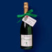 Bottle of champagne with a green ribbon and decorative tag on a blue background