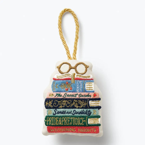 An embroidered book stack ornament featuring the titles Pride & Prejudice, Sense and Sensitivity, The Secret Garden, Harry Potter glasses, and Wuthering Heights, hanging from a gold cord on a white background.