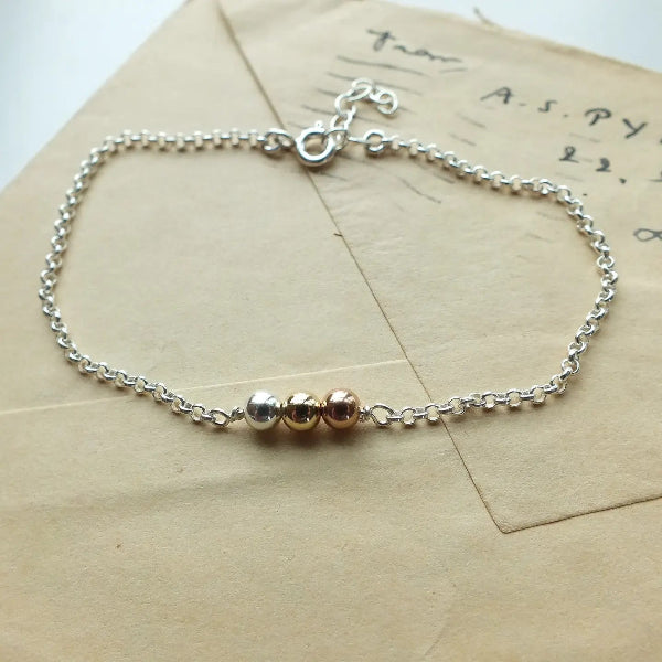Silver bracelet with gold beads on a textured surface