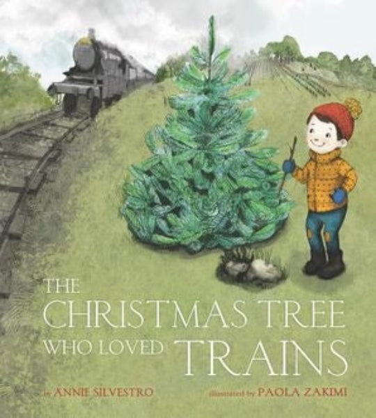 Children's book cover for 'The Christmas Tree Who Loved Trains' by Annie Silvestro, illustrated by Paola Zakmi. The cover art shows a small Christmas tree on a grassy hill next to a boy in a red beanie and yellow jacket, with a train on tracks in the background.