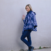 A woman posing against a light gray wall wearing a blue and white plaid hooded poncho, dark blue skinny jeans, and black boots.