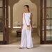 Woman in a white outfit standing in a stylish interior setting with wooden doors and neutral decor.