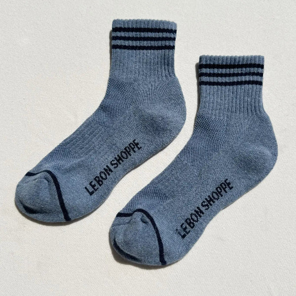 Pair of blue socks with black stripes and 'Le Bon Shoppe' branding on a light gray background