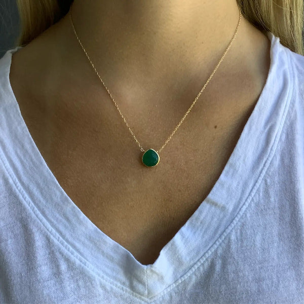 Gold necklace with a green pendant worn by a person in a white shirt.