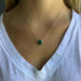 Gold necklace with a green pendant worn by a person in a white shirt.