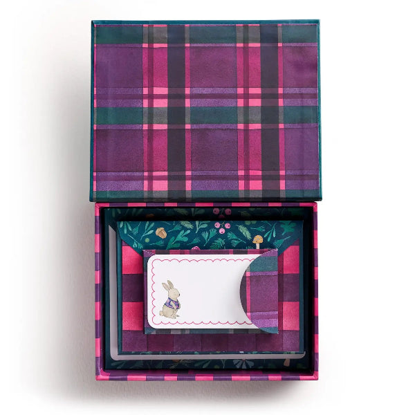 An open gift box with a purple, pink, and green plaid patterned lid and interior, containing a small white card with a bunny illustration and a matching curved insert.