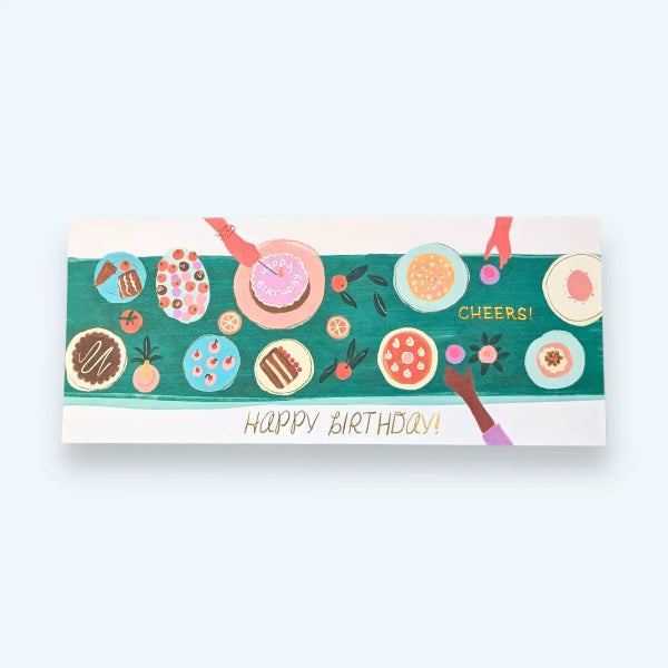 A rectangular birthday greeting card featuring a colorful illustration of a party table with plates, drinks, cake, and the words 'HAPPY BIRTHDAY!' and 'CHEERS!' on a light blue background.