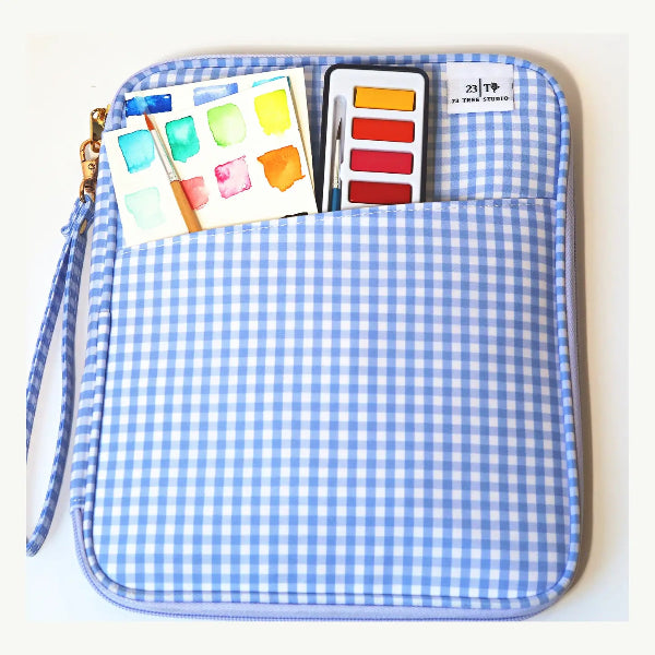 A light blue and white gingham zippered pouch with a wrist strap, shown on a white background with a watercolor palette and paint swatches peeking out of the front pocket.
