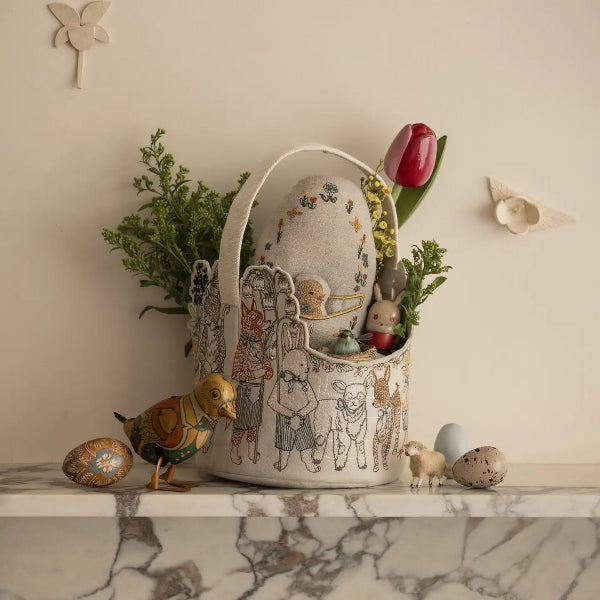 Decorative Easter basket with illustrations, flowers, and small figurines on a marble surface.