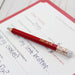 Red pencil with 'BELIEVE' on it lying on a piece of paper with writing.