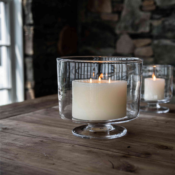 Candle in a glass holder on a wooden surface with a stone wall background