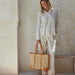 Woman holding a woven tote bag against a neutral wall