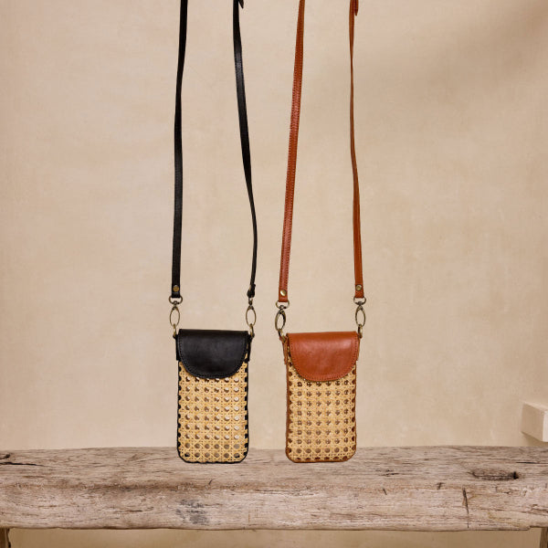 Two woven handbags with leather accents on a wooden surface against a beige wall.