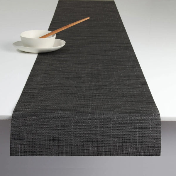 Black woven table runner on a white surface with a bowl and wooden spoon.