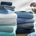 Stack of folded towels in various shades of blue and gray on a light background with a vase of flowers.