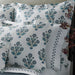 A set of white bedding pillows with a blue botanical block print pattern, styled on a bed next to a vase with dried branches.