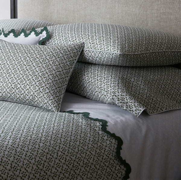 A neatly made bed with a textured green and white patterned duvet cover and matching pillow shams, accented with white pillows featuring dark green scalloped edges.