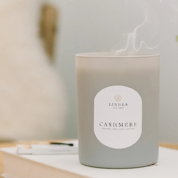 Candle labeled 'Cashmere' by LINNEA on a surface with a blurred background
