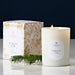 Linnea Forest Fir candle with packaging and a sprig of pine on a reflective surface.