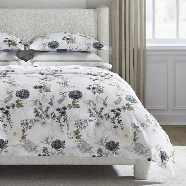 Floral bedding set on a bed in a bedroom with light-colored walls and curtains.