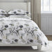 Floral bedding set on a bed in a bedroom with light-colored walls and curtains.