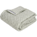 A folded quilt with a dense, small-scale abstract pattern in moss green, black, and off-white, shown on a solid white background.