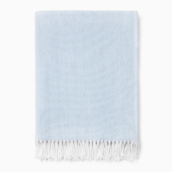 Light blue woven blanket with white fringe on a white background