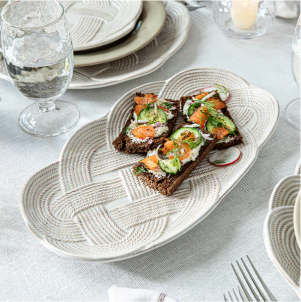 Plated sandwiches with avocado and salmon on a woven plate with a glass of water and plates in the background.
