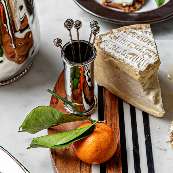 Cheeseboard with a wedge of cheese, an orange, and a small container of honey on a marble surface.