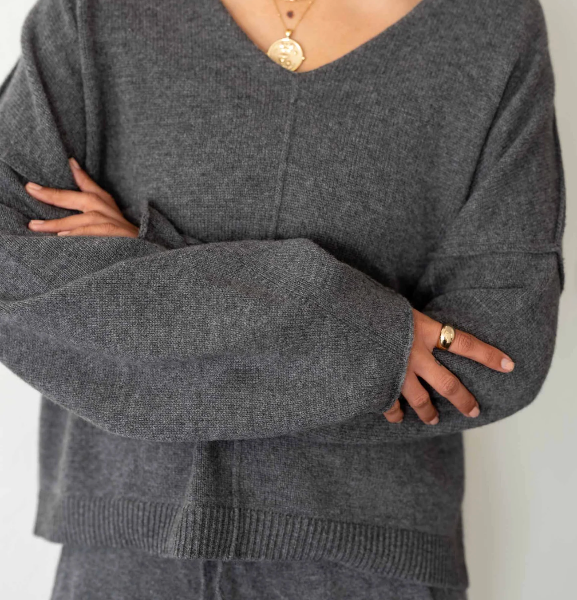Person wearing a gray sweater with arms crossed on a plain background