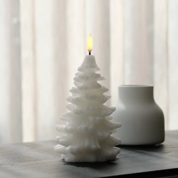 White ceramic Christmas tree candle on a table with a blurred curtain background