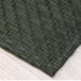 Dark green textured rug with a herringbone pattern on a light wooden floor.