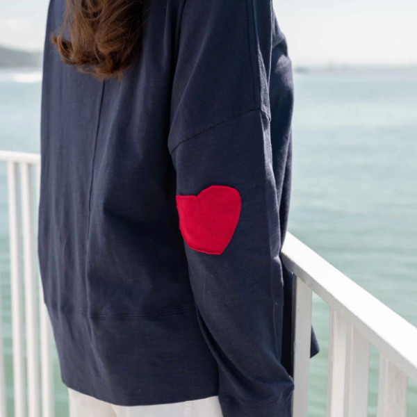 Person wearing a navy blue sweatshirt with a red heart patch on an outdoor deck.