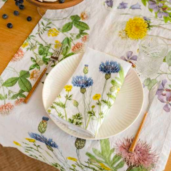 Table setting with floral-patterned tablecloth, plates, and cutlery on a wooden surface.