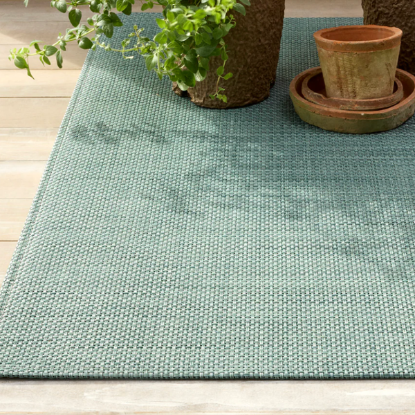 Green textured outdoor rug with potted plants on a wooden deck.