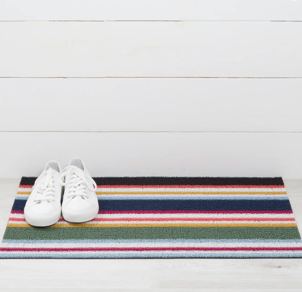 Colorful striped doormat with white sneakers on a white wooden floor