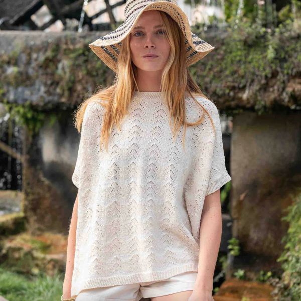 Woman wearing a white lace top and straw hat in a natural setting