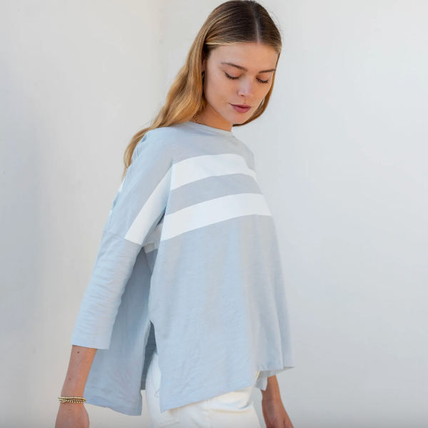 Woman wearing a light blue sweater with a white stripe on a plain background