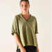 Woman wearing an olive green blouse with ruffled details on a plain background