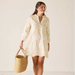 Woman wearing a white lace dress holding a woven bag against a plain background