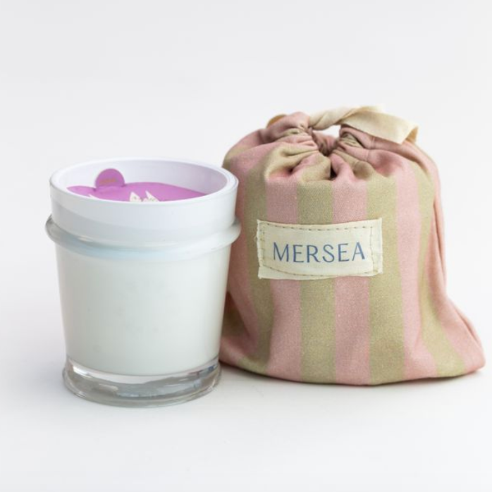 Candle in a glass jar with a striped cloth pouch labeled 'MERSEA' on a white background